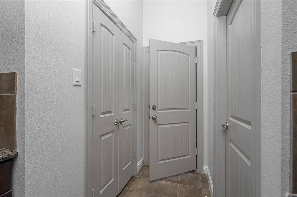 Hallway with three closed doors and one open door leading to the garage. The doors are painted in a light neutral color, and the area features tiled flooring and white walls, creating a clean and modern look.