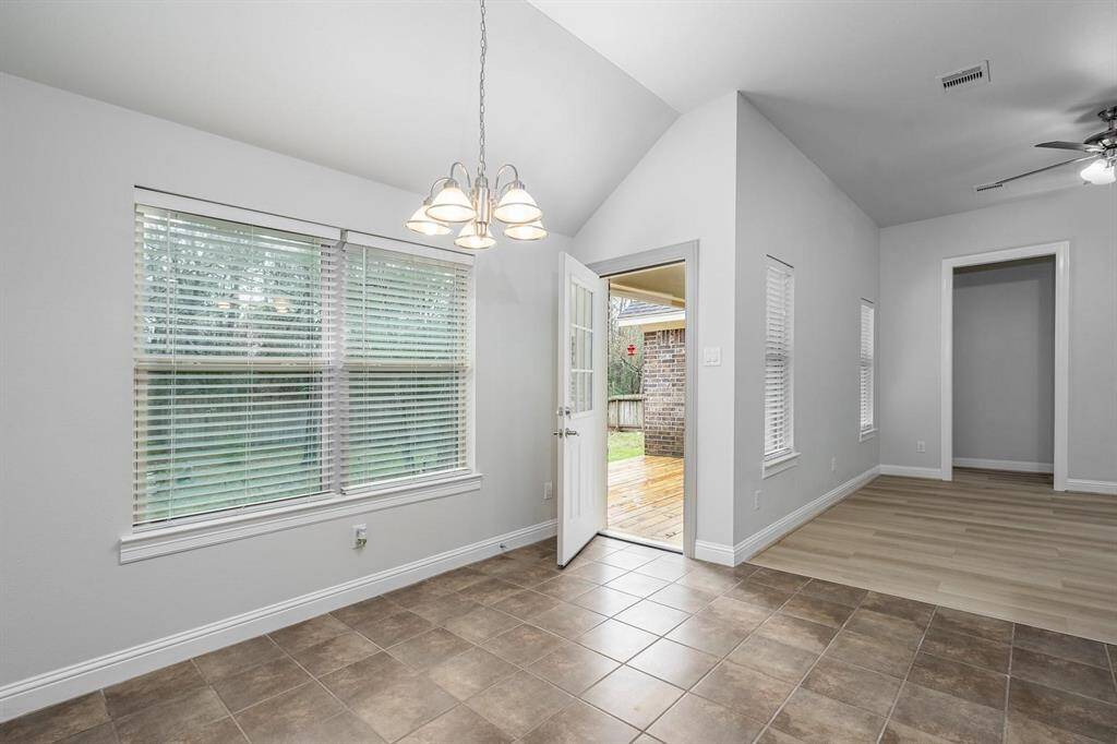 Bright, open dining area with tiled flooring, large windows, and a hanging light fixture. The room connects to a wooden deck through a glass door, and there's a transition to a space with wood-look flooring. Perfect for indoor-outdoor living.