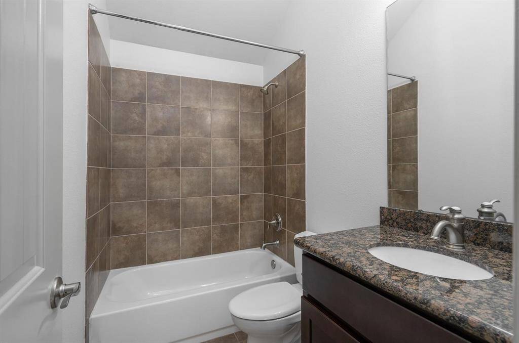 This bathroom features a tiled shower and bathtub combination, a granite countertop with an under-mount sink, a sleek faucet and tile flooring. The neutral tones create a clean and modern look, perfect for a comfortable home setting.