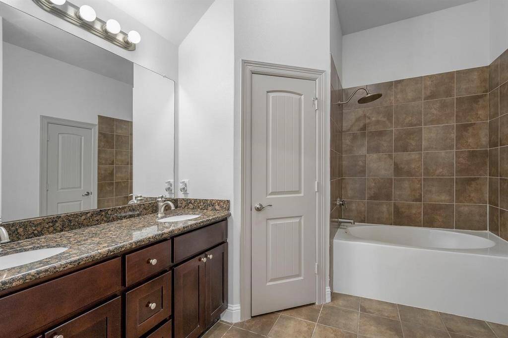 This primary bathroom features a double-sink vanity with granite countertops, a large mirror with modern lighting, and a shower-tub combo, and a separate shower with brown tile surround. The room has a neutral color palette and tile flooring.