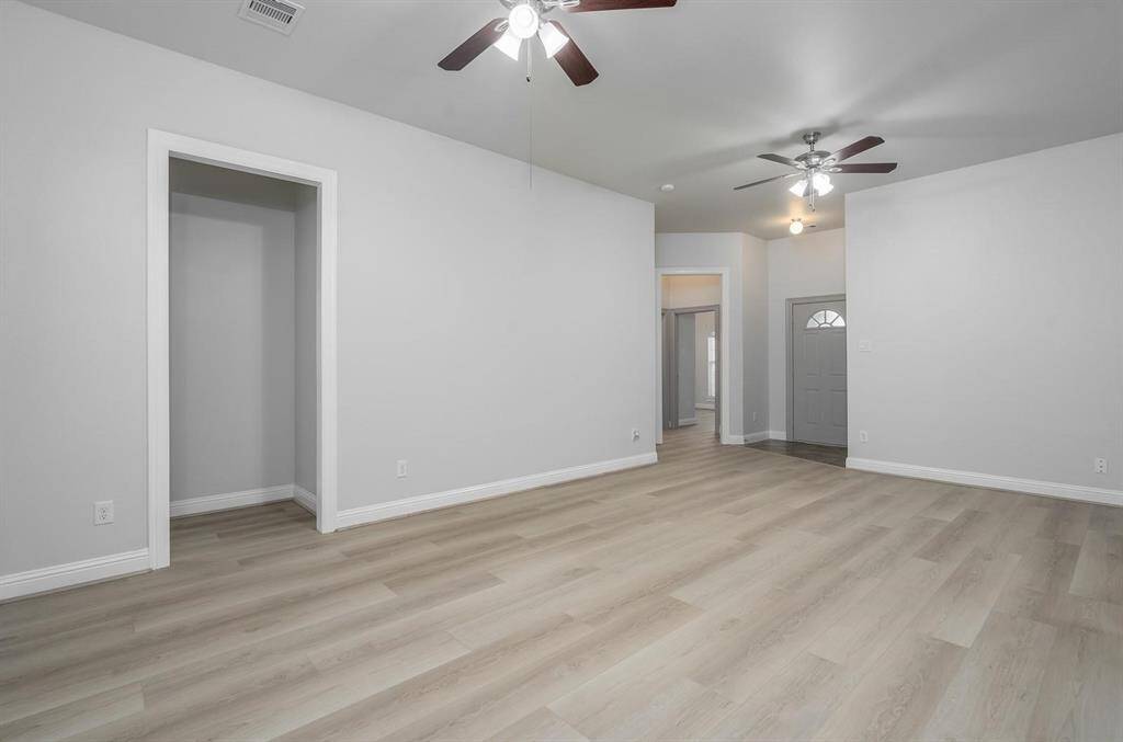 Spacious, light-filled family room with modern laminate wood flooring and neutral walls. It includes ceiling fans for comfort and an open doorway leading to additional rooms, creating a welcoming entryway.