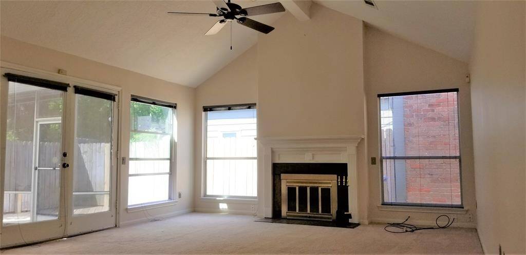 Main living area with high pitched ceiling. Wood burning fireplace, carpeting and ceiling fan.
