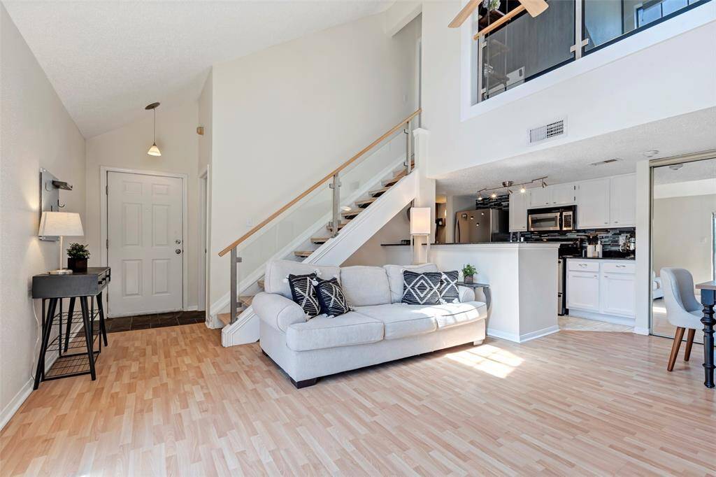 Bright living room featuring a full view of the staircase to the second floor, with a peek at the main door and a cozy kitchen tucked beneath.