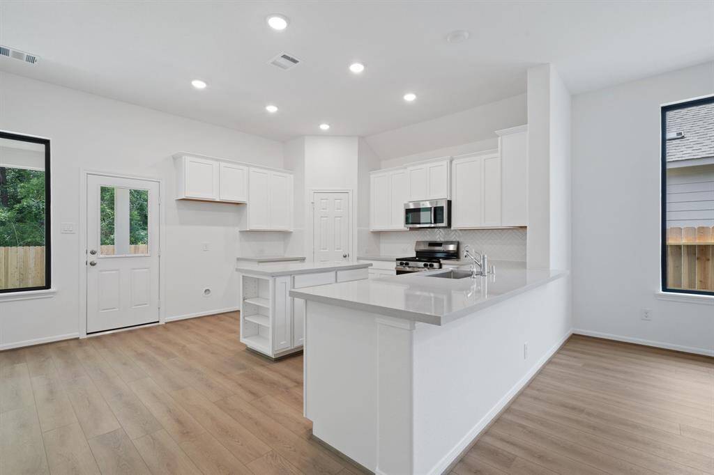 This light and bright kitchen features a large quartz island, white cabinets, a large sink overlooking your family room, recessed lighting, and beautiful backsplash.