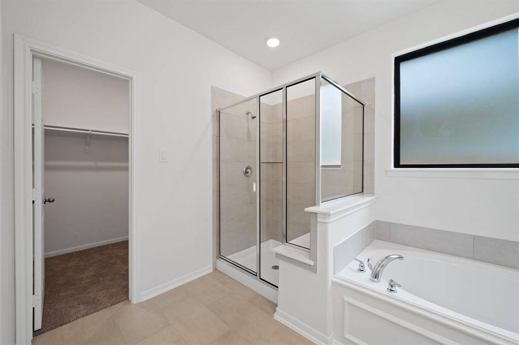 This additional view of your primary bathroom features tile flooring, fresh paint, walk-in shower, a separate garden tub, and a large walk-in closet.