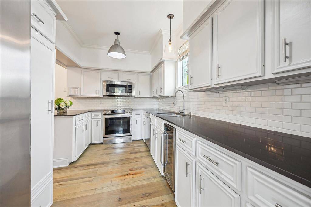 Bright, modern kitchen with white cabinetry, dark countertops, and stainless steel appliances. The kitchen features a subway tile backsplash, pendant lighting, and light wood flooring for a clean, contemporary look.