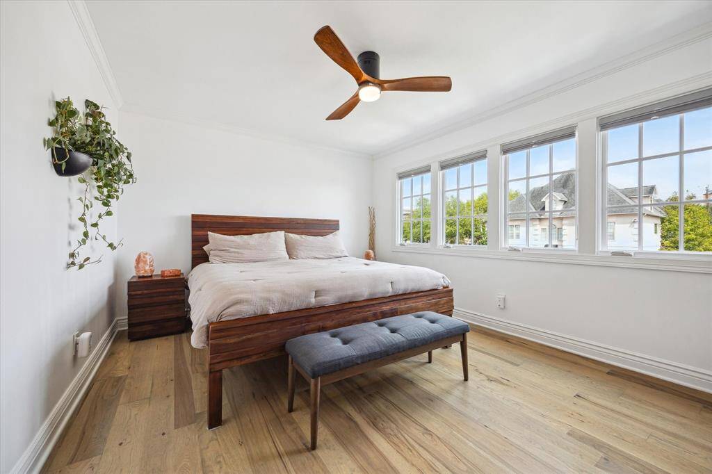 This bright and airy primary bedroom features large windows, hardwood flooring, walk-in closet and sleek ceiling fan.