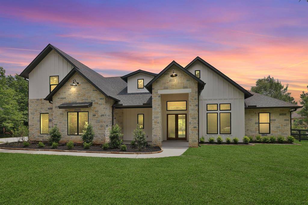 This stunning home features a modern design with a combination of stone and siding exterior. Large windows offer plenty of natural light adds to its curb appeal. warm and inviting ambiance. Grass is digitally enhanced.