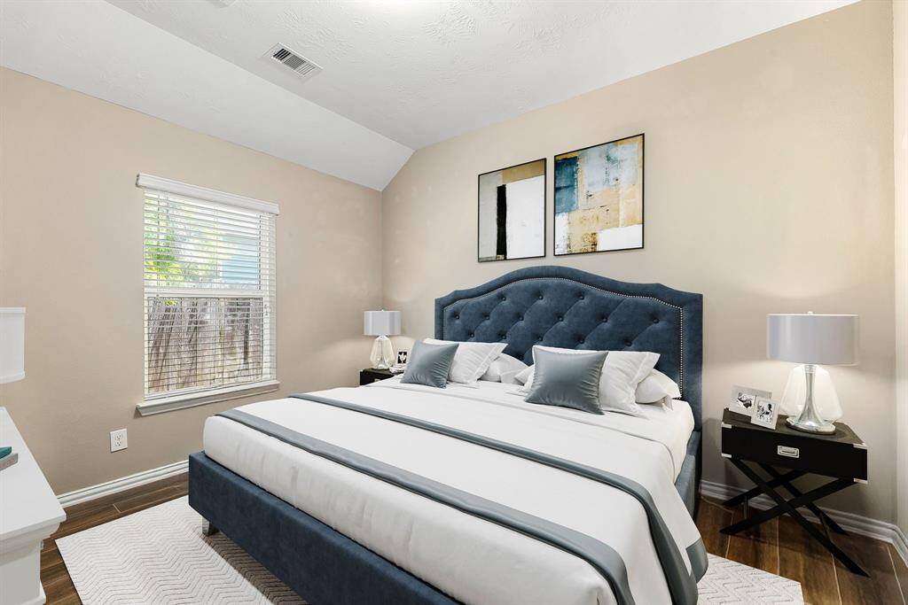 Secondary bedroom features wood style flooring, custom paint, dark stained ceiling fan with lighting and a large window with privacy blinds. *Virtually Staged