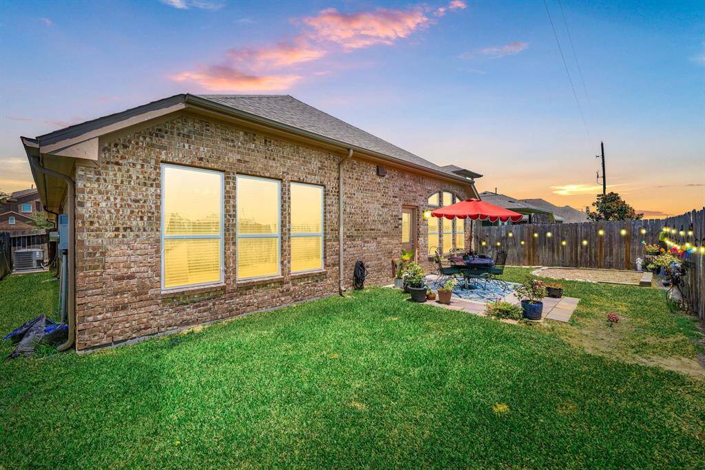 Enjoy outdoor dining and relaxing under the shade of the vibrant red umbrella on this cozy patio space, surrounded by lush greenery and potted plants.