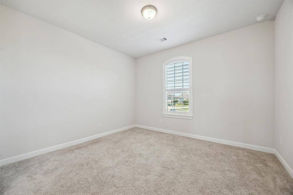 This inviting secondary bedroom is one of several designed for comfort and style, featuring plush carpeting that adds warmth and coziness. Whether used as a guest retreat, a peaceful haven for family members, or even a creative space, this room offers both versatility and charm with its custom plantation shutters.