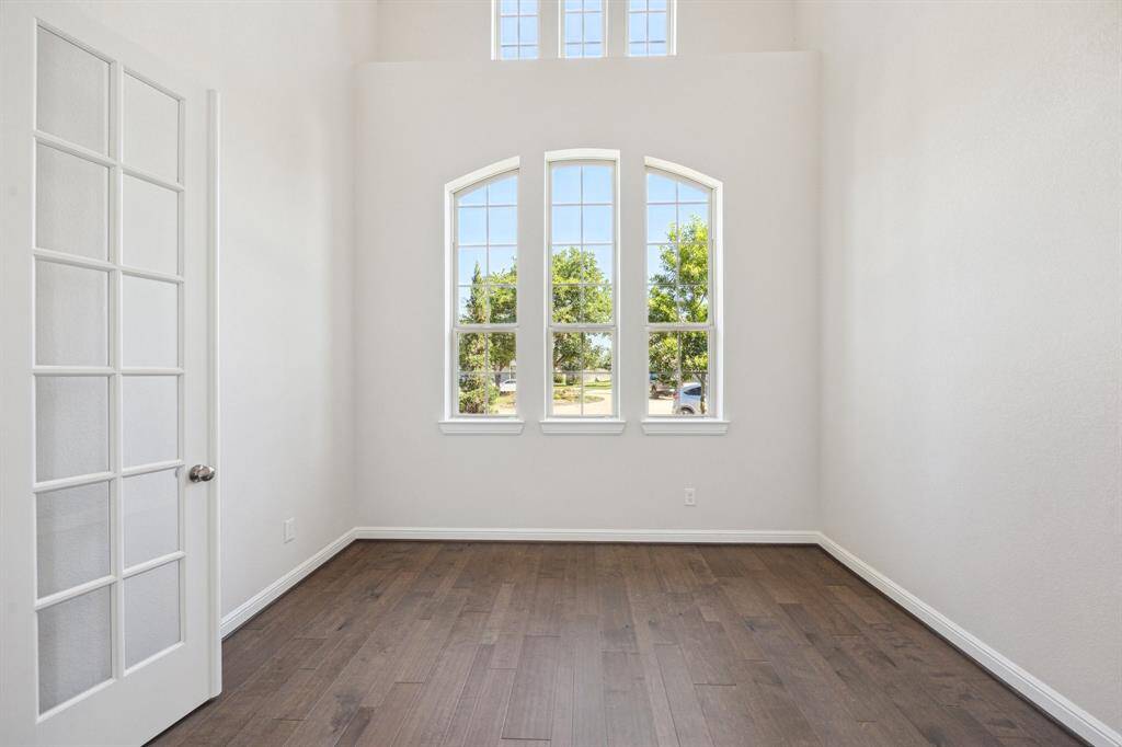 This stunning space boasts soaring ceilings and expansive windows, flooding the room with natural light and offering breathtaking views of lush landscaping beyond. Whether used as a private office or an additional living area, it provides both elegance and functionality. Perfectly situated off the grand foyer, this charming workspace or bonus room features upgraded double French doors, enhancing its sophisticated appeal.