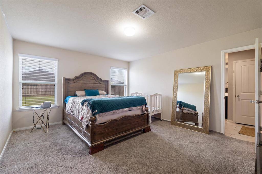 Spacious primary suite with neutral tones and soft carpet flooring, offering plenty of room for large furniture. Dual windows provide great natural light and views of the backyard. The room includes direct access to the en-suite bathroom for added convenience.