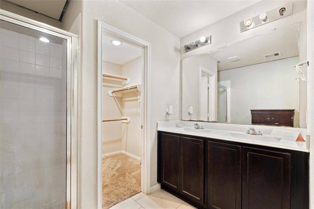 Primary en-suite bathroom featuring a dual-sink vanity with ample cabinet storage, a glass-enclosed walk-in shower, and direct access to a spacious walk-in closet.