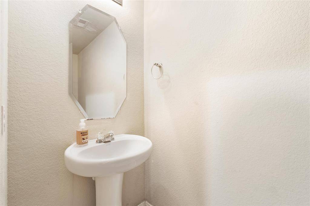 Convenient main-level half bath featuring a pedestal sink, wall-mounted mirror, and neutral tones