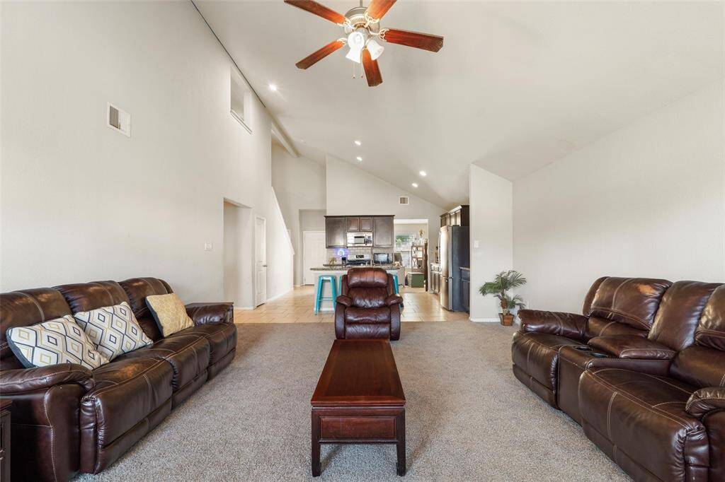 Open-concept living room with soaring vaulted ceilings, recessed lighting, and seamless flow into the kitchen. The space features a ceiling fan and ample room for large-scale seating. Ideal for entertaining or relaxing with family.