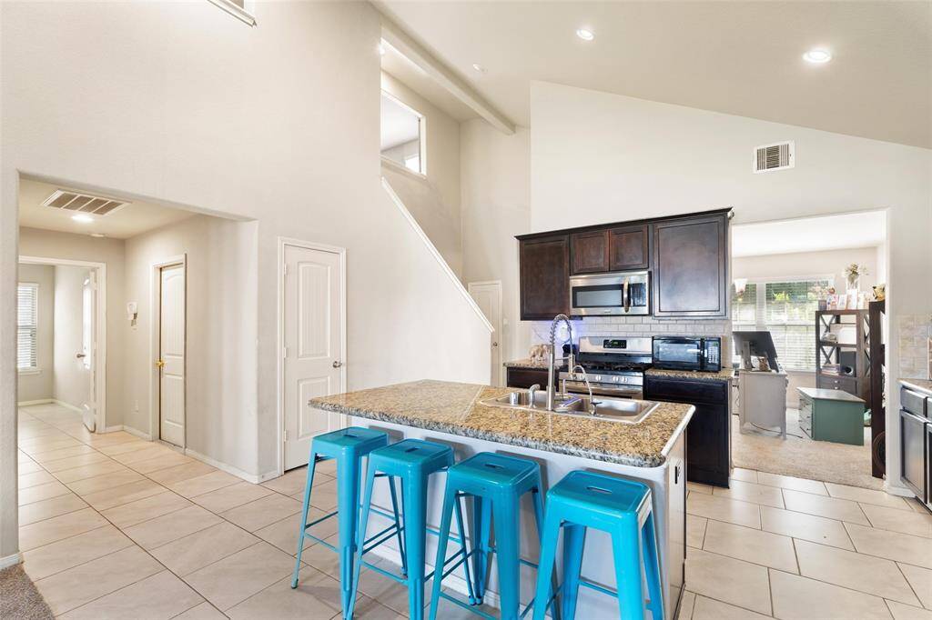 Stylish kitchen with granite countertops, a center island with breakfast bar seating, and stainless steel appliances. The open layout offers clear sightlines into the adjacent flex room and hallways, while neutral tile flooring and recessed lighting add a modern touch.