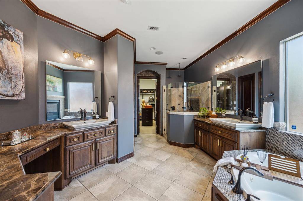 This luxurious primary bedroom is a serene retreat, enhanced by soaring double-height ceilings and elegant architectural details. A dual-sided fireplace adds both warmth and sophistication, beautifully shared between the bedroom and the spa-like primary bathroom, offering comfort and ambiance in both spaces.