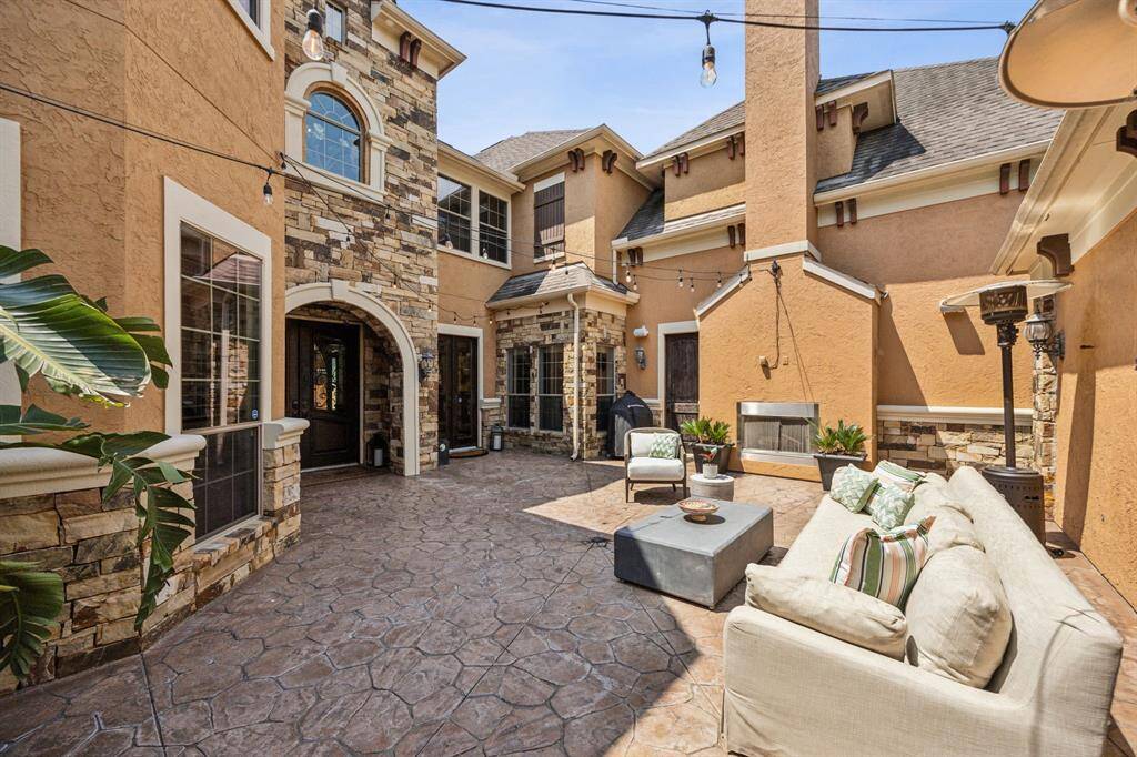 This photo highlights a generously sized home exterior featuring a textured stone courtyard, framed by stucco walls and numerous large windows. The architecture blends gabled and hip rooflines, while a striking wooden front door with an arched entryway adds a touch of elegance and warmth.