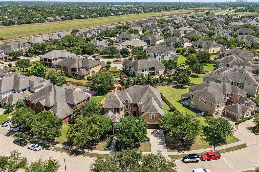 This stunning aerial view showcases the home’s impressive presence within a beautifully maintained neighborhood, surrounded by other elegant, well-appointed residences. The expansive lot, complete with a sparkling pool, stands out as a true gem, highlighting the home’s premier location and the overall charm of this desirable community.