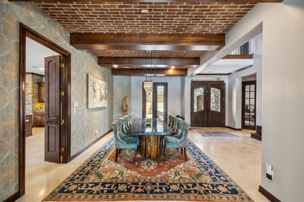 This photo captures a sophisticated interior featuring a sweeping curved staircase with wooden railings and wrought iron balusters. Abundant natural light pours in through large windows and French doors, illuminating the tiled floors and creating a warm, welcoming entryway.