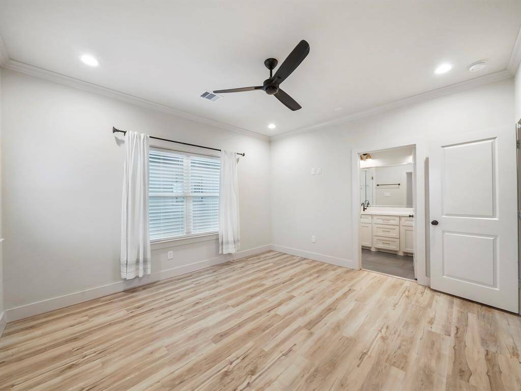 A different view of the primary bedroom with en-suite bathroom.  Modern ceiling fan and luxury vinyl plank flooring.