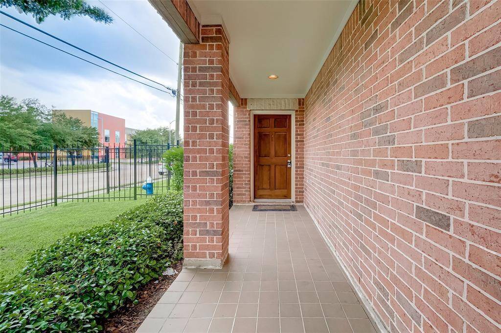 A covered hallway runs alongside the home, open on the side that’s bordered by brick pillars and greenery, creating a lovely approach to the main entrance.