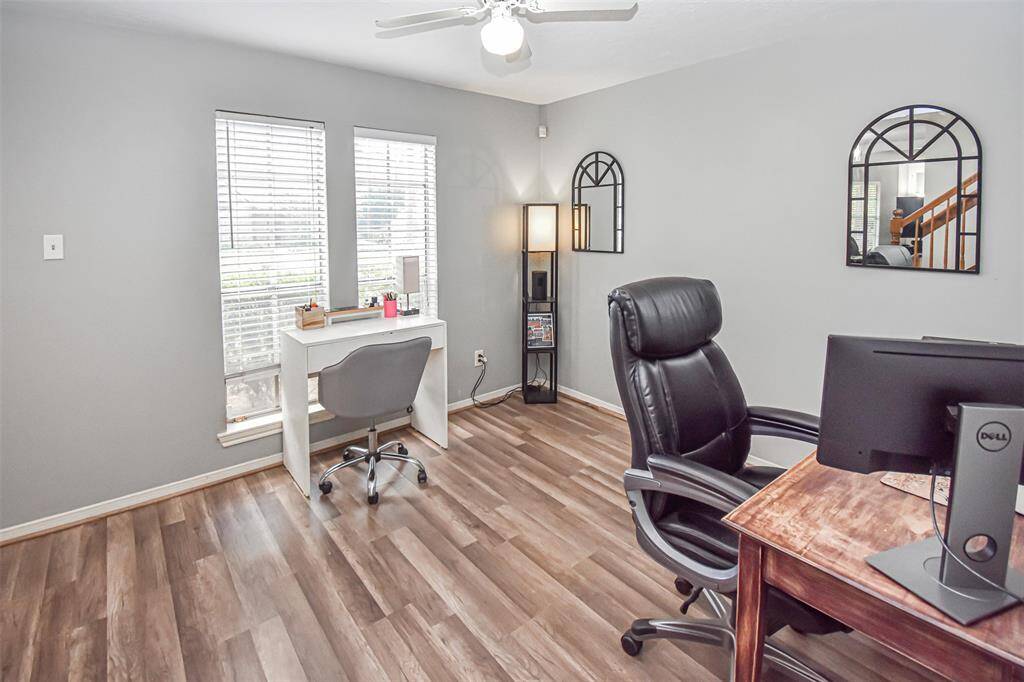 This bright home office with large windows, modern flooring, and a ceiling fan. It features two desks, ample lighting, and a stylish design—ideal for productivity.
