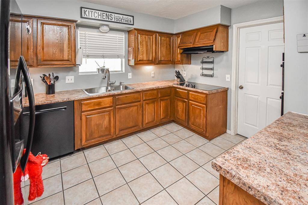 This kitchen features warm wood cabinetry, plenty of counter space, and neutral tile flooring. It includes a double sink, black appliances, and ample counter space, creating a functional and inviting cooking area.