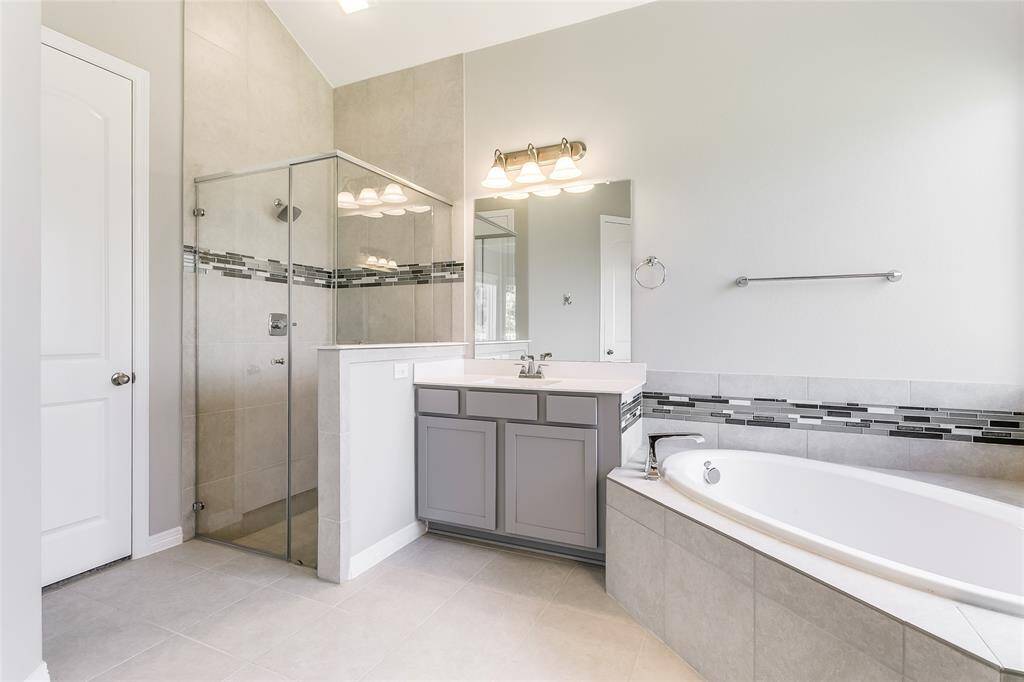Another view of this Elegant Primary Oasis that is accompanied with a spacious glass enclosed shower, sink with beautiful gray cabinetry, and Large soak tub!