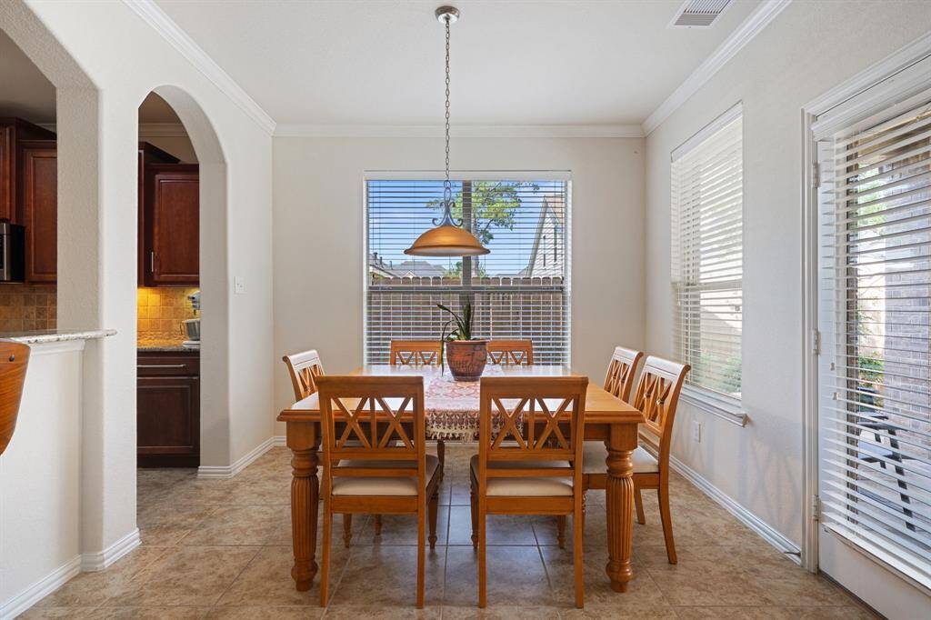 This spacious dining room includes a pendant lighting, tile floors, crown molding details, and windows with privacy blinds.