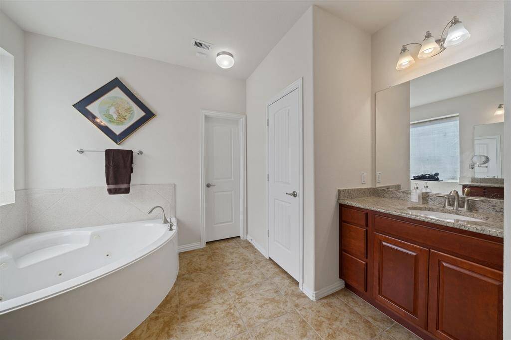 This master bathroom is highlighted by a jetted tub, tile floors, walk-in closet, granite countertops and backsplash.