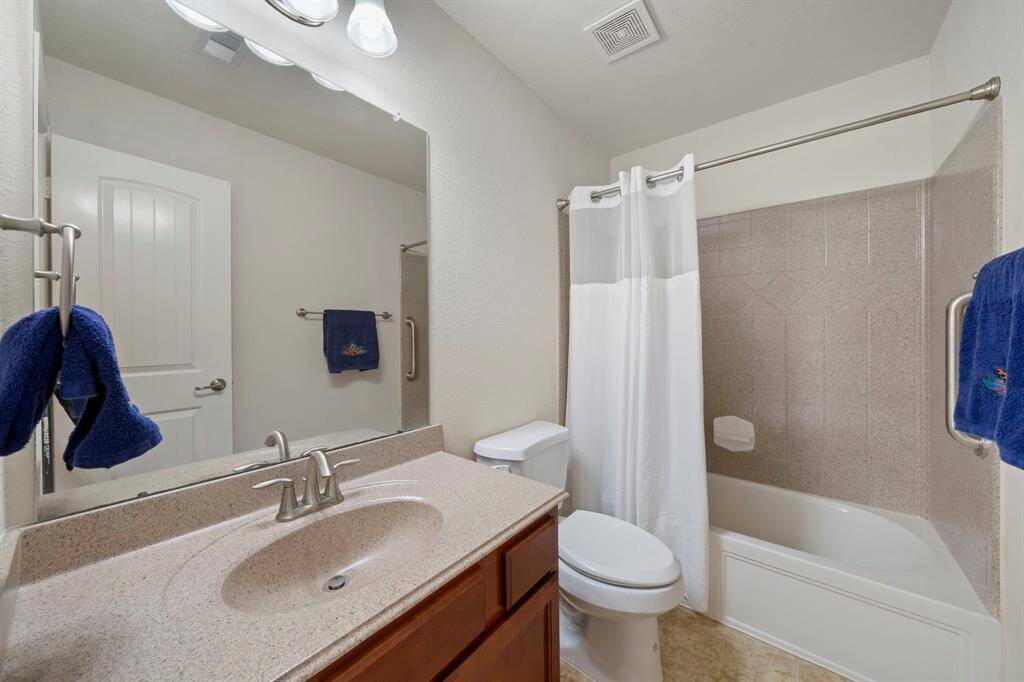 Secondary bathroom with shower/tub combo, tile floors, corian countertops and backsplash, and a large mirror.