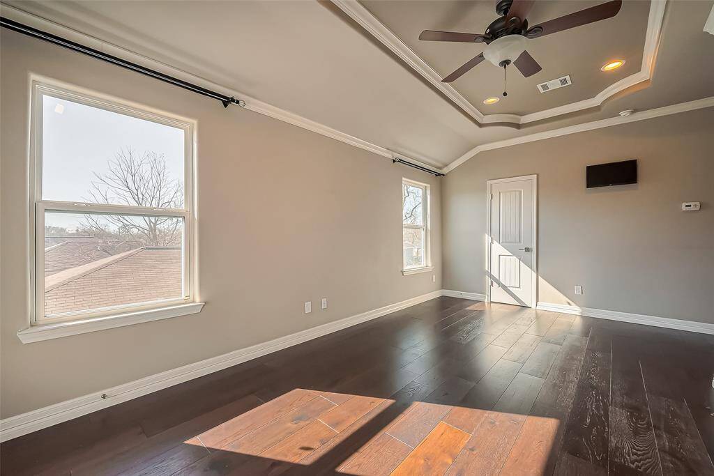 This primary bedroom has wonderful natural lighting, with a ceiling fan and a light kit. There is also dark laminate throughout the room.