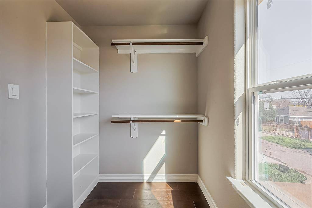 You do not see a closet with dark laminate floors every day. This primary closet has built-in shelves, double rods with natural light coming through the window.