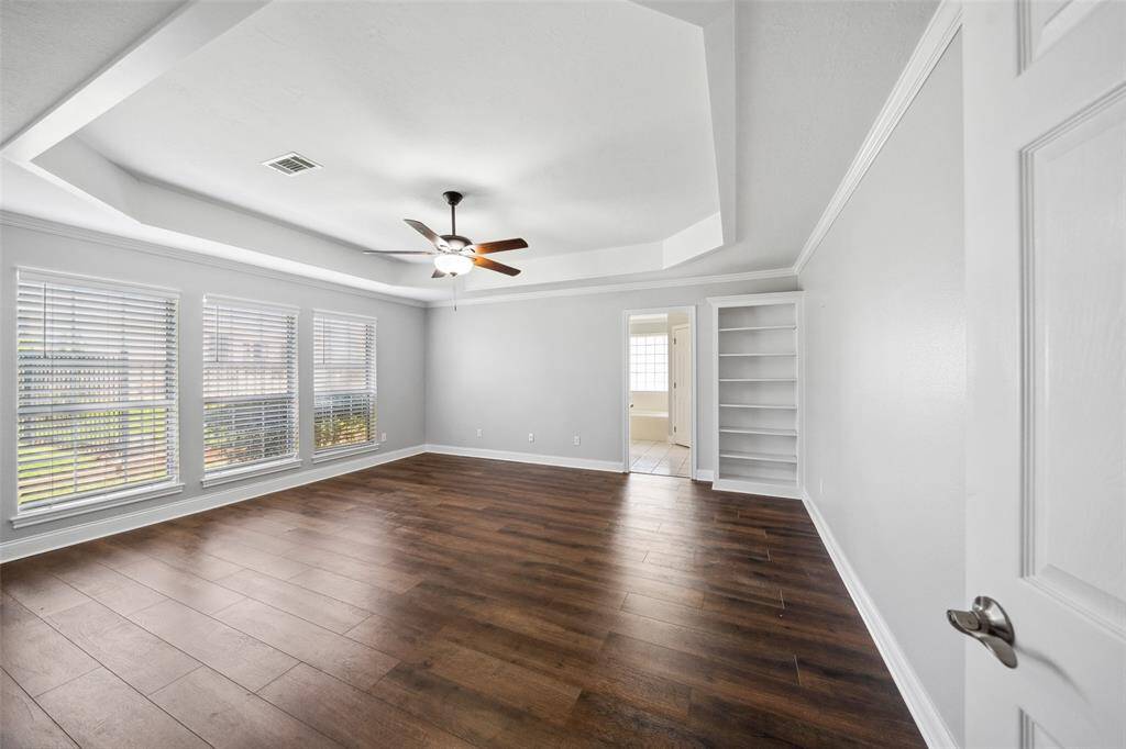 Large master bedroom with raised ceiling, wood flooring, and extra built-in cabinet.