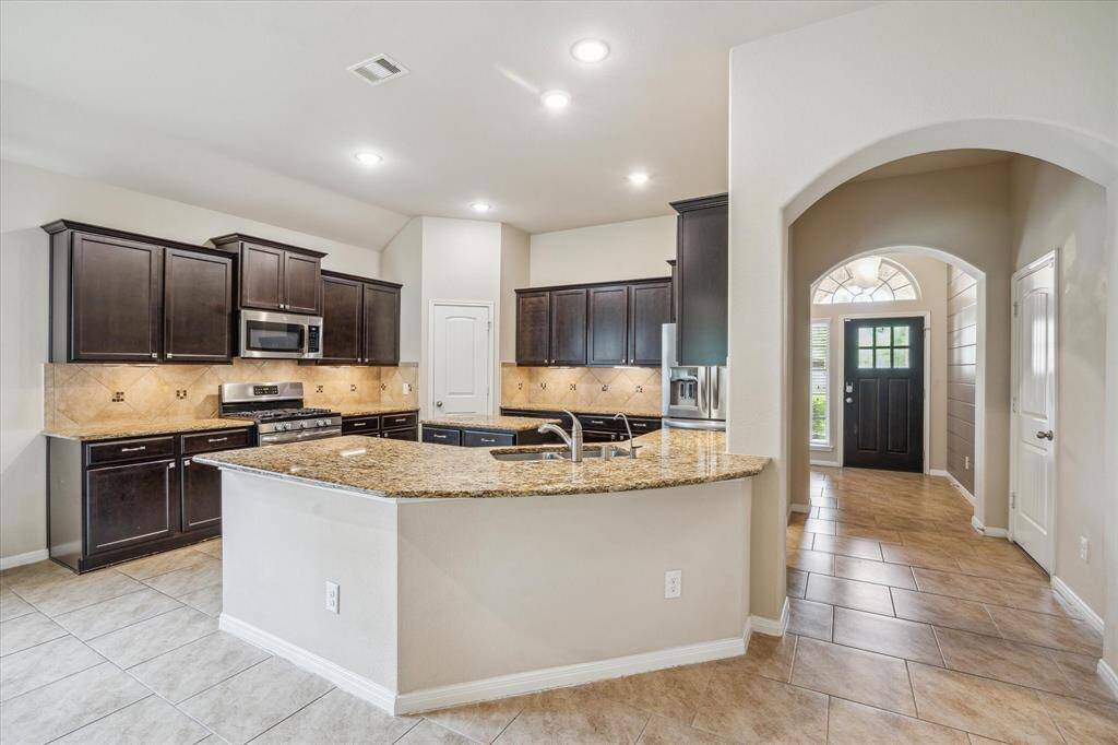 This spacious kitchen features dark wood cabinets, granite countertops, under cabinet lighting, pantry, and stainless steel appliances.