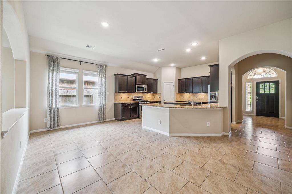 This photo shows a spacious, open-concept kitchen and dining area with tiled floors. Large windows provide natural light to your dining room table.