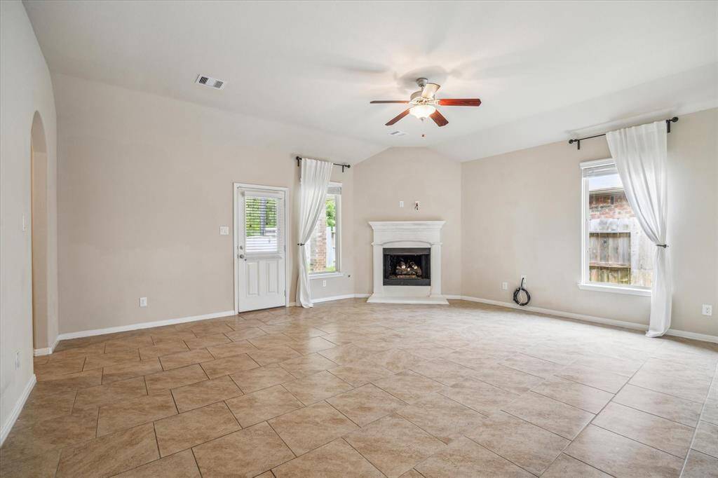 Spacious family room featuring a cozy fireplace, elegant tile flooring, and abundant natural light from large windows. Perfect for relaxation and entertainment.