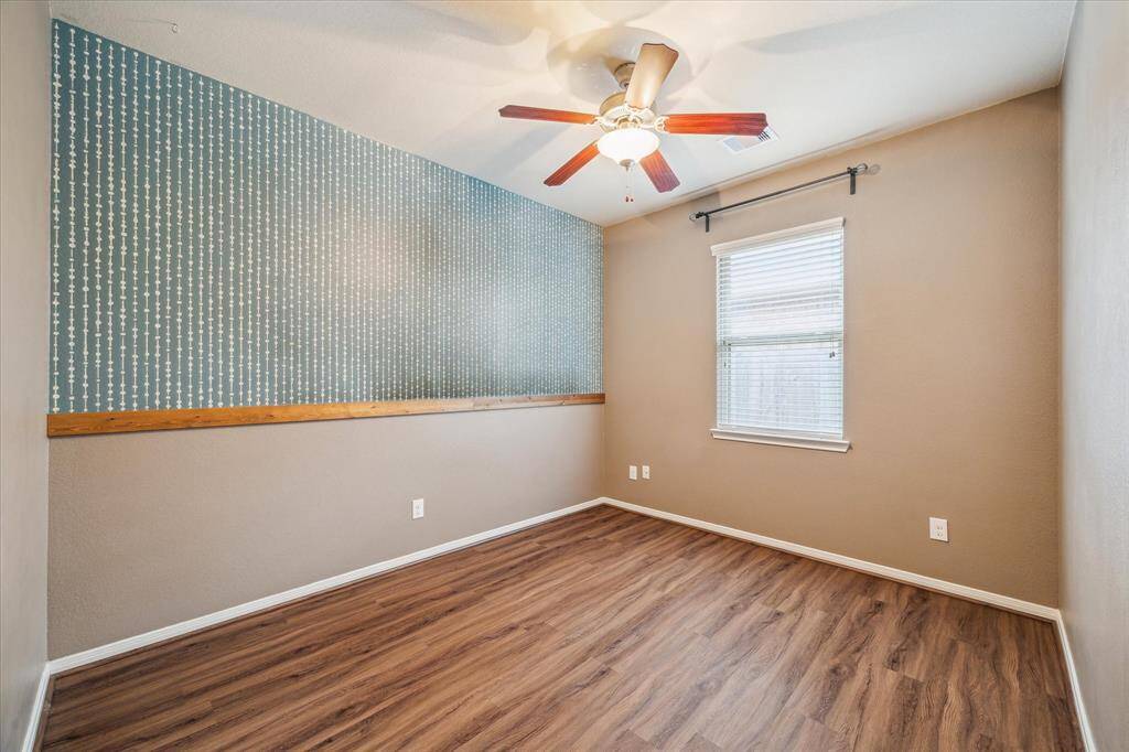 This secondary bedroom features a unique accent wall with blue patterned wallpaper, and neutral paint on the other walls, creating a cozy atmosphere. Walk in closet with sleek modern shelving.