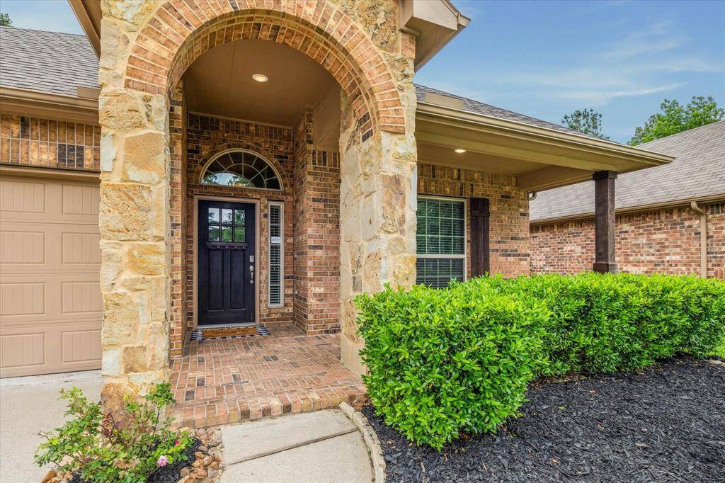 Charming brick and stone exterior with an inviting arched entryway, complemented by well-maintained landscaping and a cozy front porch.