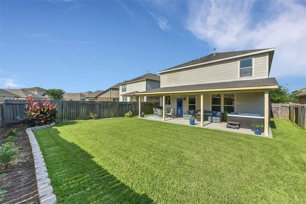 This picture showcases the good size of the backyard, enhanced by a practical sprinkler system and charming new flower beds. Your eye is also drawn to the inviting covered patio