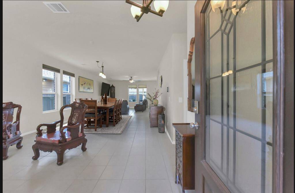As the door opens, a glimpse into the home reveals a combined formal living and dining area, with a partial view extending into the main living space.