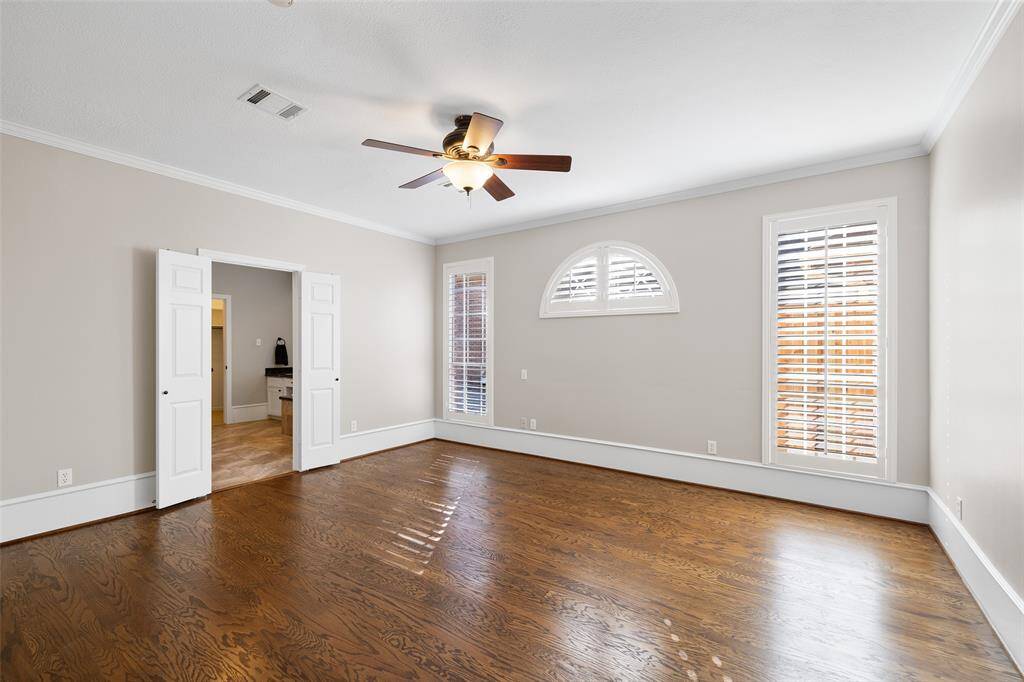 Large primary bedroom with attractive windows with plantation shutters and wood flooring.