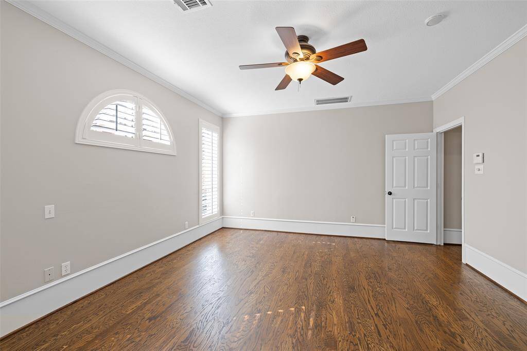 Another view of large primary bedroom with polished wood flooring and high ceiling with ceiling fan.