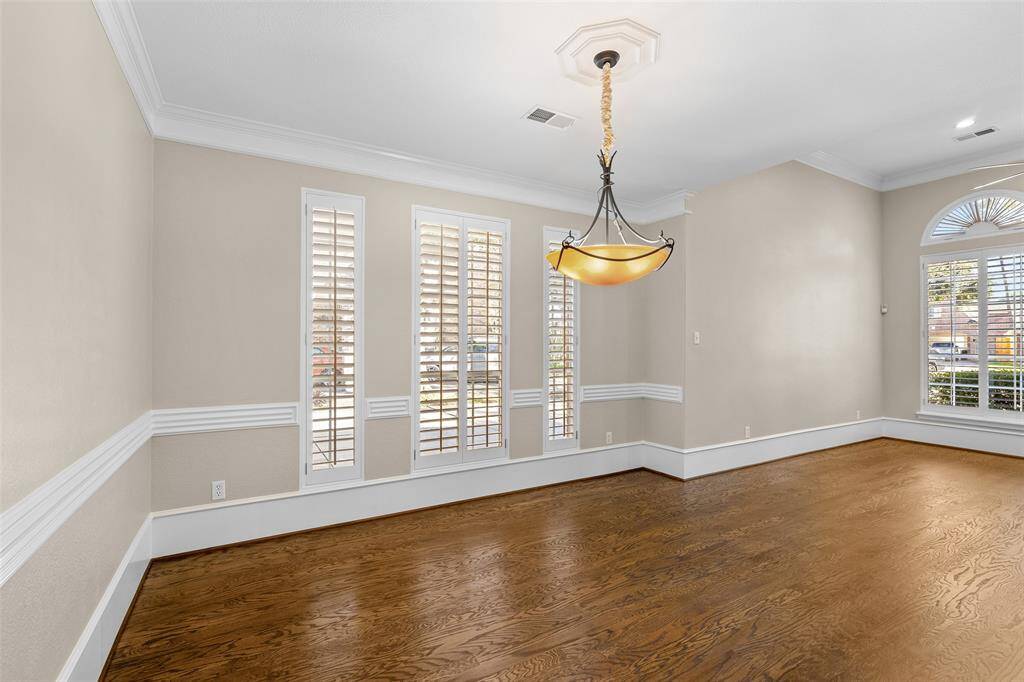 Another view of spacious well-lit room featuring polished wood floors, chair rails and an attractive chandelier serving as the centerpiece for lighting.