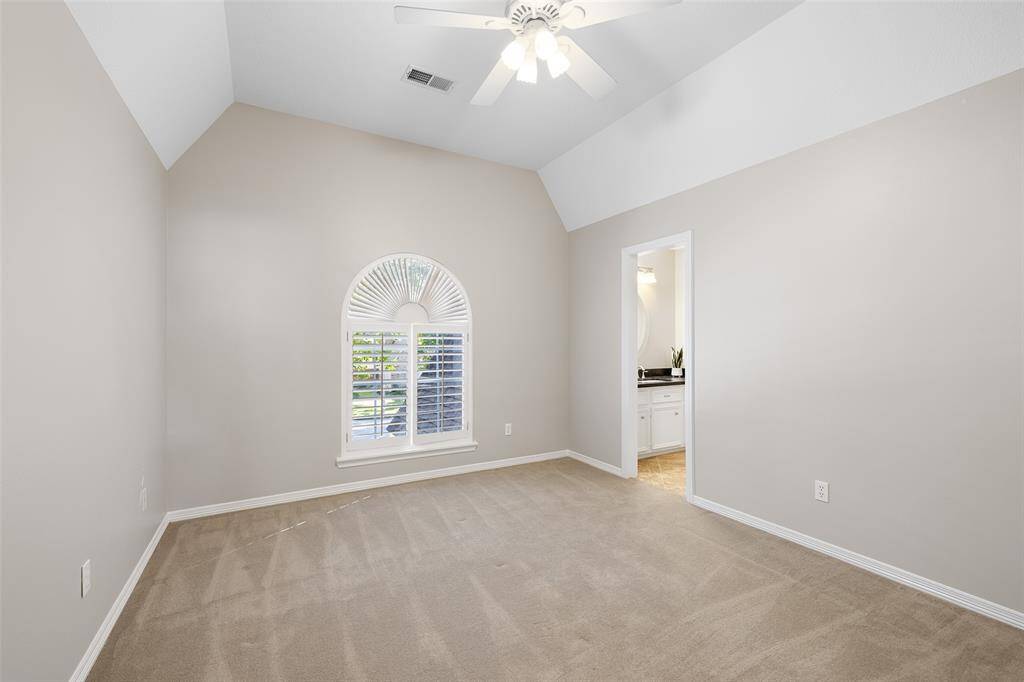 Large secondary upstairs bedroom with arched ceiling and arched window with plantation shutters showing entrance to Jack & Jill bathroom.