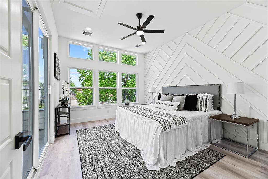 This bright, modern primary bedroom shines with a stylish chevron-patterned accent wall and big windows that let in plenty of natural light. A sleek ceiling fan keeps things comfortable, and sliding glass doors open to a balcony—perfect for a peaceful moment outdoors. Spacious and inviting, it’s a room that feels like your own calm retreat.