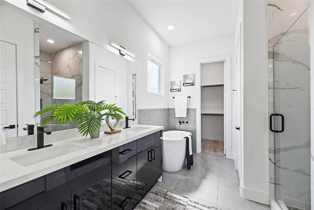 This modern bathroom blends style and comfort effortlessly. You’ve got a sleek double vanity with black fixtures, a roomy walk-in shower accented with marble, and a freestanding tub that invites you to unwind. Bright, airy, and dressed in neutral tones, the space feels fresh and relaxing thanks to contemporary lighting that sets the perfect mood.
