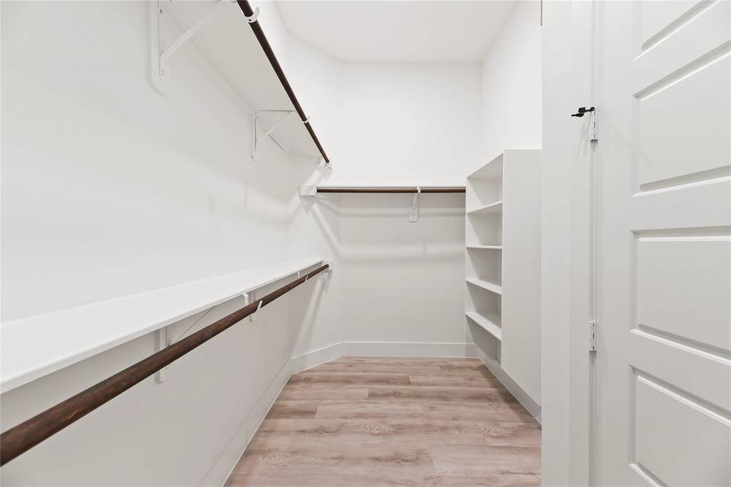 Spacious walk-in closet with light wooden flooring, multiple hanging rods, and built-in shelving, ideal for organized storage.